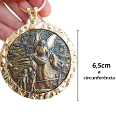 Medalhão de berço em formato redondo com imagem de anjo da guarda em relevo, medindo 6,5 cm de circunferência.