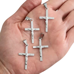 Quatro pingentes em formato de cruz de aço com figura de Cristo, segurados na palma da mão.