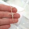 Colar cruz Cristo folheado em ouro, segurado na mão, com detalhes em brilho.