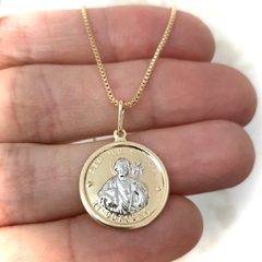 Colar folheado em ouro com medalha de São Judas, segurado na mão.