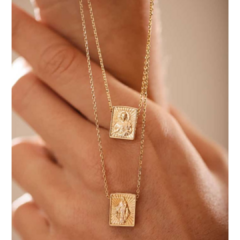 Escapulário Nossa Senhora do Carmo em estilo retangular, com detalhes em dourado, pendurado em uma mão.