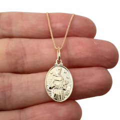 Colar folheado a ouro com medalha de São Francisco, segurado por uma mão.