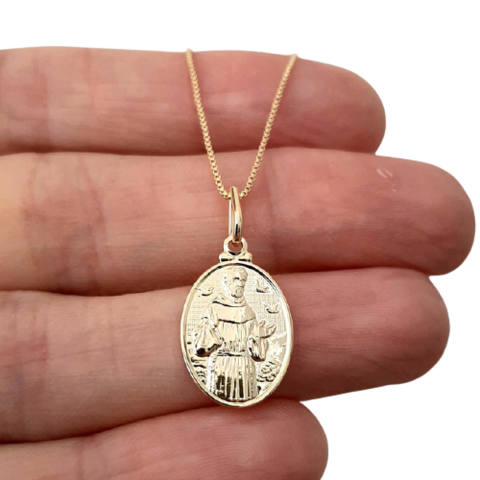 Colar folheado a ouro com medalha de São Francisco, segurado por uma mão.