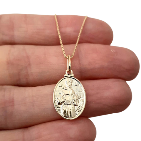 Colar folheado a ouro com medalha de São Francisco, segurado por uma mão.