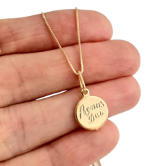 Colar folheado a ouro com pingente Agnus Dei sendo segurado na mão.