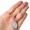Colar de medalha milagrosa em aço, com detalhes visíveis, segurado na mão.