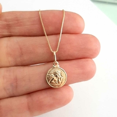 Colar folheado com medalha pequena de anjo, segurado na mão.