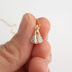 Colar folheado com pingente em forma de Nossa Senhora Aparecida, sendo segurado por uma mão.