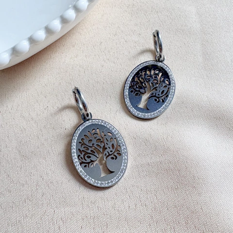 Brinco de argola com pingente em formato de árvore da vida, feito em aço inox hipoalergênico, sobre fundo de tecido claro.