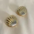 Brinco de concha dupla em metal com acabamento dourado, exibindo um design elegante e texturizado.