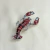 Broche em formato de lagosta vermelha com base prateada. Um acessório estiloso e ousado, perfeito para dar um toque divertido ao look.