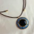 Colar com cordão e medalhão em ouro envelhecido, com pedras azuis, douradas e resina redonda preta. Estilo marcante, ideal para quem ama peças com personalidade.