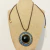 Colar com cordão e medalhão em ouro envelhecido, com pedras azuis, douradas e resina redonda preta. Estilo marcante, ideal para quem ama peças com personalidade.