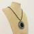 Colar com cordão e medalhão em ouro envelhecido, com pedras azuis, douradas e resina redonda preta. Estilo marcante, ideal para quem ama peças com personalidade.