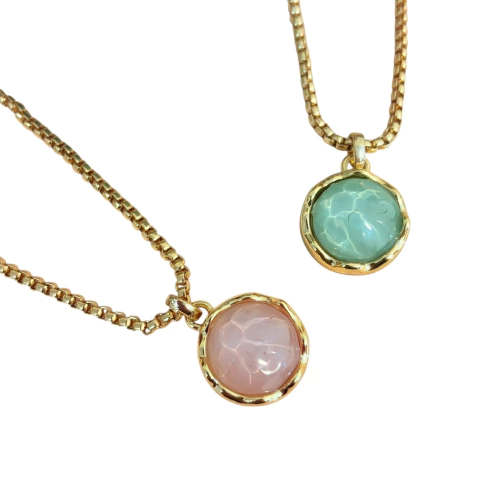Colar com pingente redondo em pedra acrílica com efeito aquático, disponível em azul claro ou rosa claro. Cordão dourado com banho de verniz italiano.