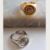 Anéis de dedinho de metal com design espiral, um dourado e um prateado, sobre uma superfície clara.
