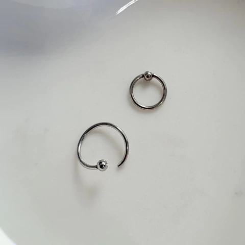 Piercing captive de torção em aço prateado 0,8 mm, hipoalergênico e versátil. Ideal para nariz, orelha, septo e outros furos. Resistente e fácil de usar.