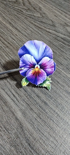 Die cut en forma de flor pensamiento con detalles en tonos púrpura, azul y amarillo sobre fondo de madera