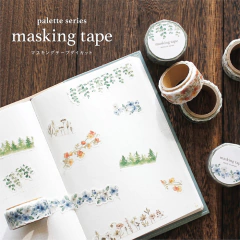 Rollos de washi tape troquelado con diseños de flores y plantas colocados sobre un cuaderno abierto con muestras pegadas