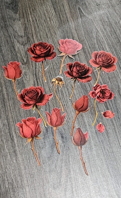 Die cuts de papel con diseños vintage de rosas rojas en distintos estados de floración sobre fondo de madera gris.