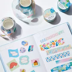 Rollo de sticker PET SODA clear de 30 mm de ancho con diseños coloridos y abstractos, mostrado junto a ejemplos de stickers aplicados en un cuaderno.