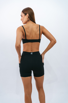 Mulher de costas usando shorts slim preto da marca Lurk, com alças finas e detalhes nas costas.