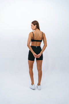 Modelo feminina usando o Top Slim Preto Lurk, visto de costas, com short preto e tênis brancos, em um fundo neutro.
