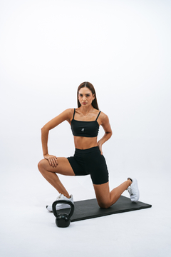 Modelo feminina usando top slim preto da marca Lurk, posando em uma superfície de treino com um kettlebell ao lado.