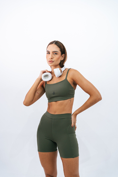 Mulher usando top verde com headphone e shorts, exibindo um estilo atlético.