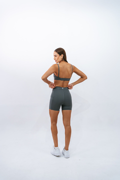 Mulher usando um top slim escuro e short curto, com vista de costas, em um fundo branco.