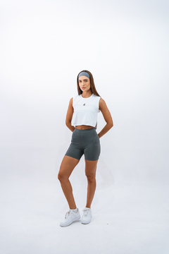 Modelo usando regata cropped branca da marca Lurk, combinada com shorts cinzas e tênis brancos, em fundo neutro.
