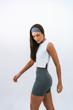 Modelo feminina usando regata cropped branca e shorts cinza, com cabelo solto e faixa na cabeça.