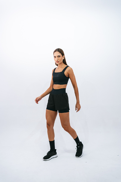 Modelo usando o top preto Lurk e shorts pretos, em um fundo branco.