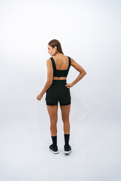 Modelo vista de costas usando o Top Core Preto Lurk, com short preto e tênis, em fundo branco.