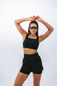 Modelo usando top preto e shorts da marca Lurk, com óculos escuros, em fundo branco.