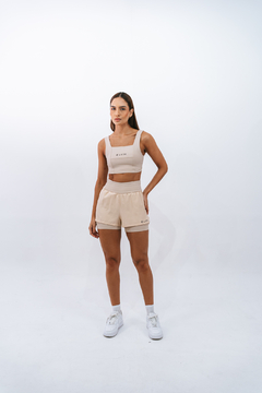 Modelo vestindo top e short de esporte na cor bege, com a marca LURK estampada.