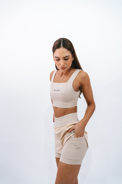 Modelo vestindo shorts Core Bege/Duna Lurk, em um fundo branco, destacando detalhes do produto.