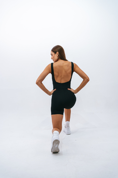 Macaquinho feminino preto com costas abertas, modelo em ação durante um exercício.