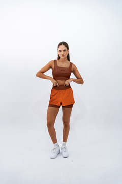 Modelo vestindo top e short na cor âmbar da marca Lurk, em fundo branco.