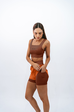 Modelo usando top e shorts âmbar da marca Lurk, com detalhes em marrom, em um fundo claro.