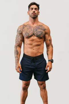 Modelo masculino exibindo boardshorts marinho da marca Lurk, com tatuagens visíveis no corpo.