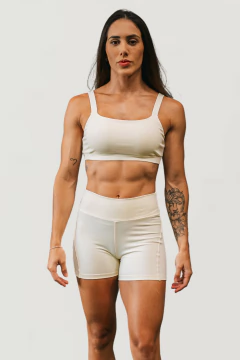 Modelo feminina usando um conjunto de treino natural na cor creme, composto por top e shorts.
