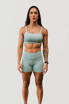 Modelo feminina usando shorts recortados na cor verde claro e top esportivo, ideal para atividades físicas.