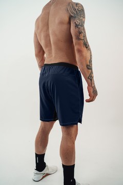 Homem musculoso visto de costas usando shorts esportivo azul marinho com detalhes em branco e tênis branco