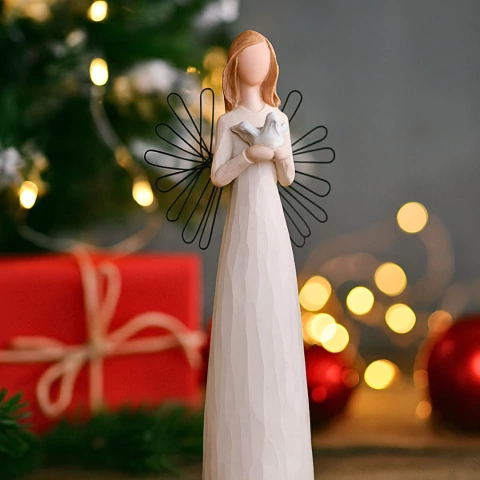 Estatueta de anjo segurando uma pomba, com asas de arame preto, em fundo com luzes de Natal e presentes vermelhos desfocados