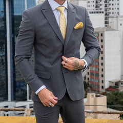 Hombre vestido con traje formal slim fit gris oscuro, corbata amarilla con puntos y pañuelo amarillo en el bolsillo.