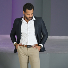 Hombre vistiendo un blazer petróleo slim fit con camisa blanca y pantalones claros, posando en un entorno moderno.