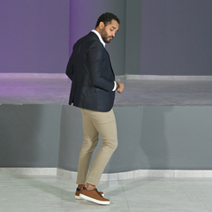 Hombre vistiendo un blazer petróleo slim fit con pantalón beige y zapatillas marrones, de espaldas en un entorno moderno.