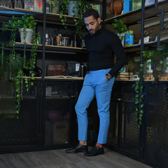 Hombre con pantalones azules y camiseta negra, de pie frente a una estantería con plantas y utensilios de cocina.