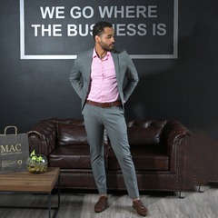 Hombre con traje gris y camisa rosa, posando en una oficina moderna con un sofá marrón y un cartel en la pared.
